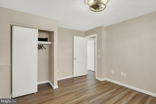 unfurnished bedroom with wood finished floors, baseboards, and a closet