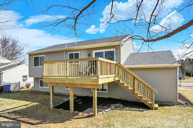 rear view of house with a shingled roof, fence, stairway, a wooden deck, and a lawn