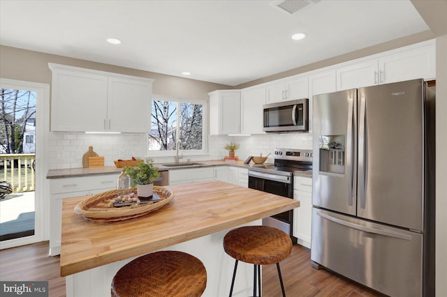 kitchen featuring butcher block countertops, stainless steel appliances, dark wood-style floors, white cabinetry, and a sink