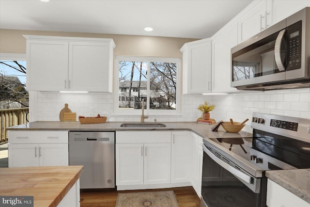 kitchen with dark wood-style floors, a sink, decorative backsplash, appliances with stainless steel finishes, and white cabinetry