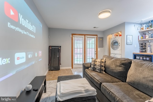 living area with visible vents, stacked washer and clothes dryer, electric panel, light tile patterned floors, and baseboards