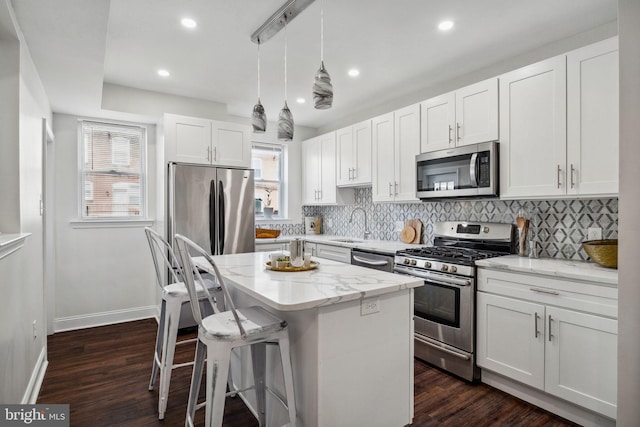 kitchen with a center island, light stone counters, decorative backsplash, appliances with stainless steel finishes, and white cabinetry