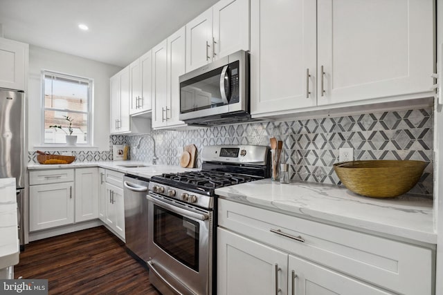 kitchen with a sink, light stone counters, dark wood-style floors, stainless steel appliances, and white cabinets