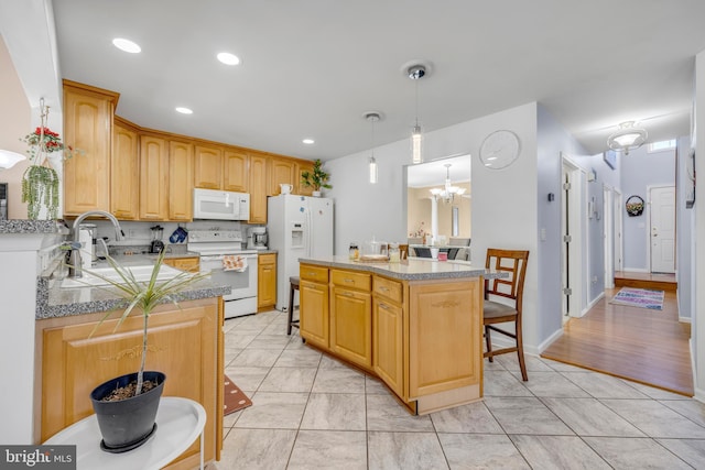 kitchen featuring white appliances, a breakfast bar area, a kitchen island, decorative light fixtures, and a notable chandelier