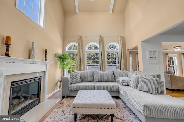 living area featuring a glass covered fireplace, a towering ceiling, ceiling fan, and wood finished floors