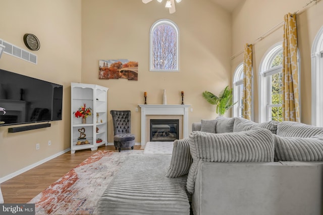 living room with visible vents, wood finished floors, a glass covered fireplace, a high ceiling, and baseboards