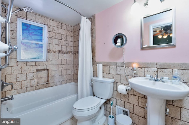 bathroom featuring visible vents, toilet, shower / bath combo, tile walls, and wainscoting