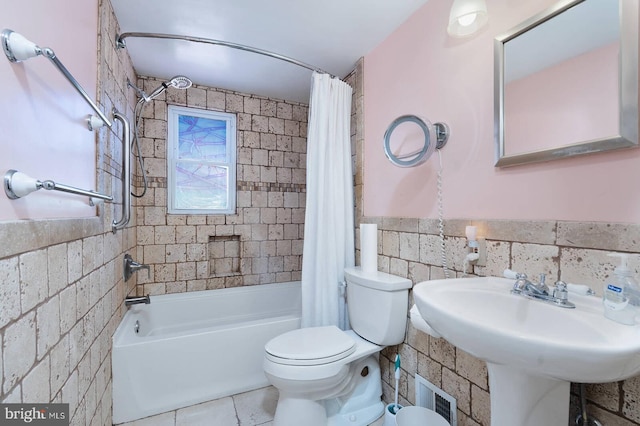 full bath with a wainscoted wall, toilet, tile walls, and shower / tub combo