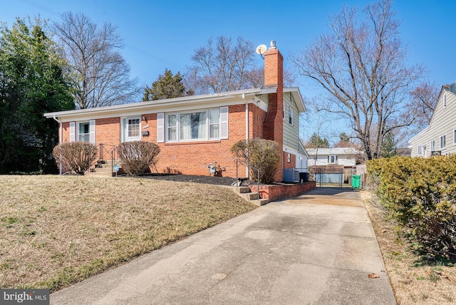 ranch-style home with brick siding, a front lawn, a chimney, driveway, and a gate