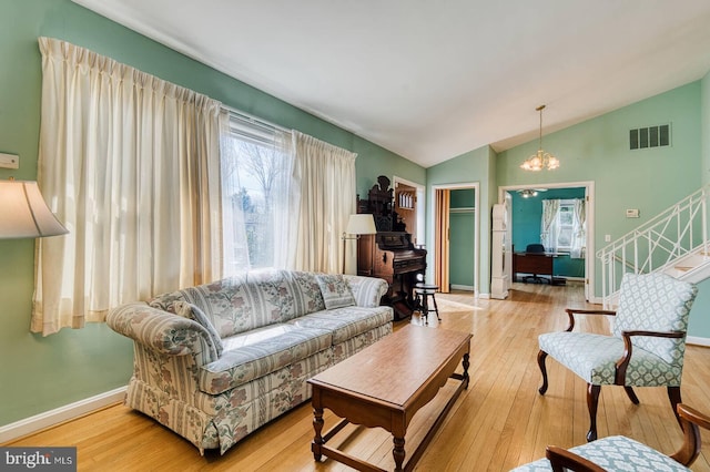 living area with hardwood / wood-style flooring, a notable chandelier, visible vents, and lofted ceiling