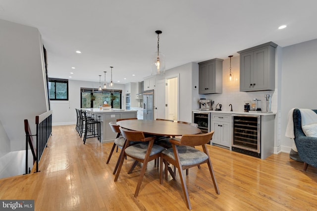 dining area with indoor wet bar, recessed lighting, beverage cooler, and light wood finished floors