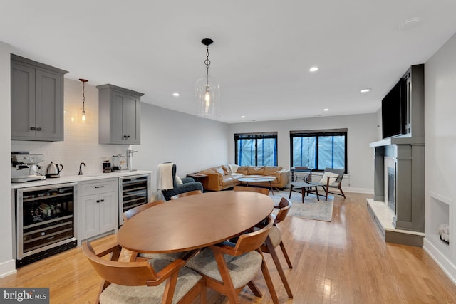 dining room featuring indoor wet bar, baseboards, beverage cooler, and light wood finished floors