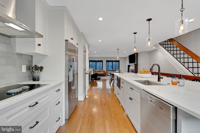 kitchen with light wood-type flooring, a sink, open floor plan, stainless steel appliances, and wall chimney exhaust hood