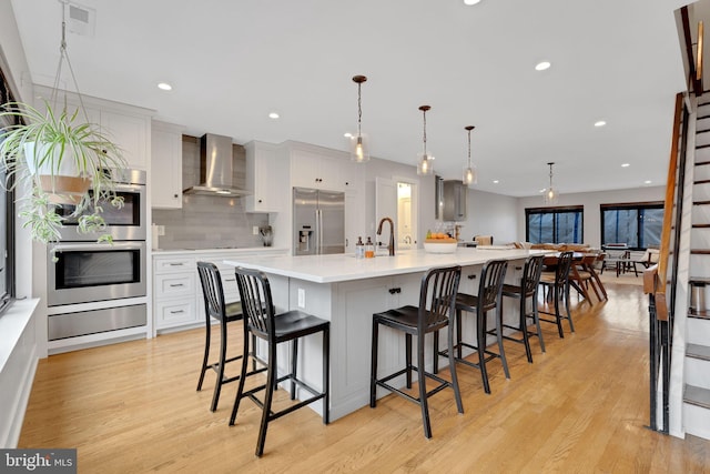 kitchen with a warming drawer, light wood-style flooring, stainless steel appliances, wall chimney exhaust hood, and light countertops