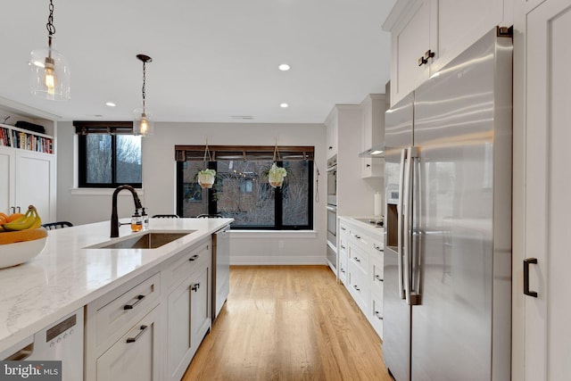 kitchen with appliances with stainless steel finishes, white cabinetry, light wood-type flooring, and a sink