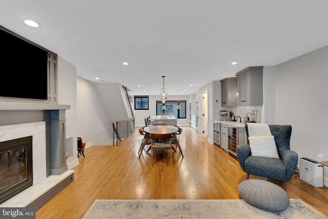 dining area with baseboards, recessed lighting, a high end fireplace, wine cooler, and light wood-type flooring