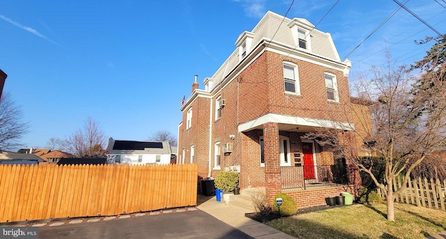 view of front of home with brick siding, fence, a front yard, central AC unit, and mansard roof