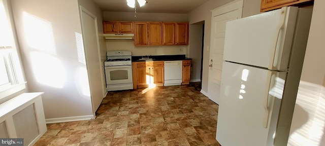 kitchen featuring white appliances, dark countertops, baseboards, and under cabinet range hood