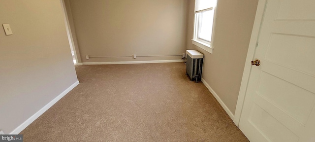 carpeted spare room featuring radiator and baseboards