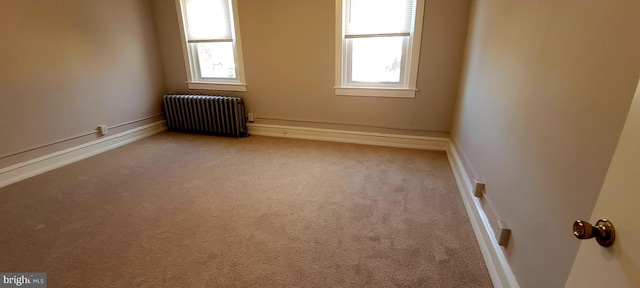 carpeted empty room featuring radiator, baseboards, and a wealth of natural light