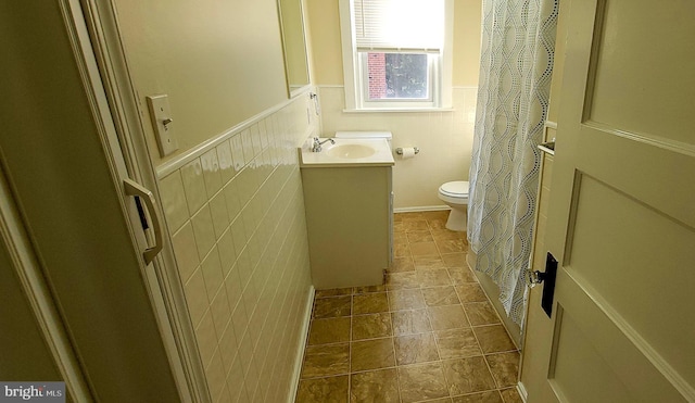 bathroom featuring vanity, toilet, tile walls, and wainscoting