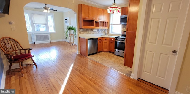 kitchen featuring backsplash, radiator heating unit, appliances with stainless steel finishes, light wood-style floors, and arched walkways