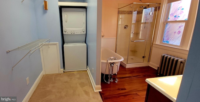 clothes washing area featuring laundry area, radiator, and stacked washer / drying machine