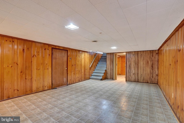 finished basement featuring tile patterned floors, wood walls, and stairs