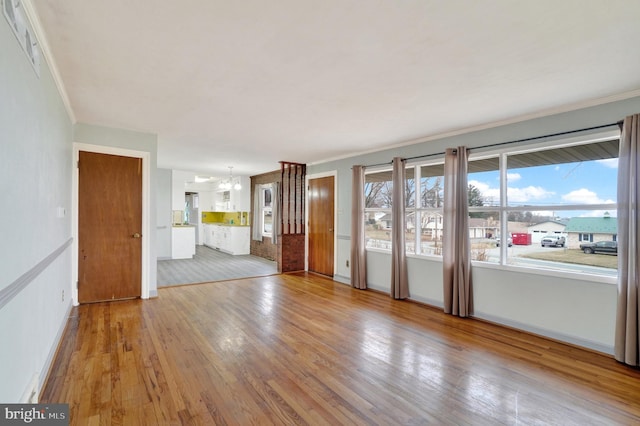 unfurnished room with a notable chandelier, crown molding, baseboards, and wood-type flooring