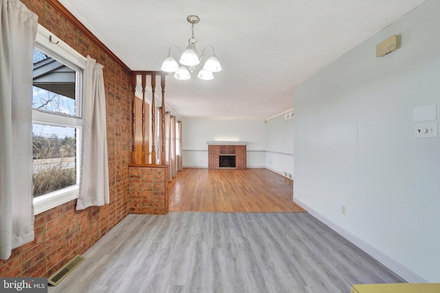 unfurnished living room with a notable chandelier, visible vents, brick wall, and wood finished floors