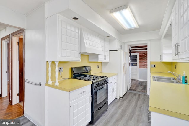 kitchen featuring light wood finished floors, black range with gas stovetop, light countertops, white cabinetry, and a sink