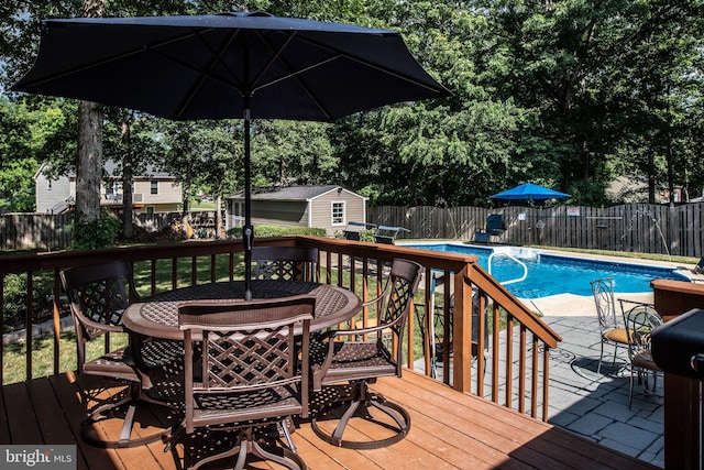 deck with a fenced in pool, an outdoor structure, outdoor dining area, and a fenced backyard