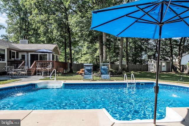 outdoor pool with a fenced backyard, a shed, a yard, an outdoor structure, and a wooden deck