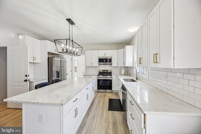 kitchen with a kitchen island, a sink, light wood-style floors, appliances with stainless steel finishes, and backsplash