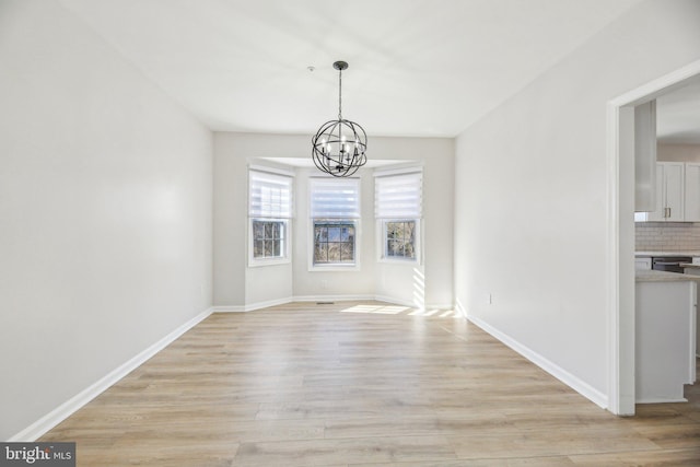 unfurnished dining area with light wood-type flooring, baseboards, and a chandelier