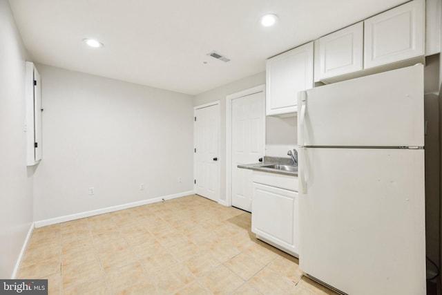 kitchen featuring visible vents, baseboards, freestanding refrigerator, white cabinets, and a sink