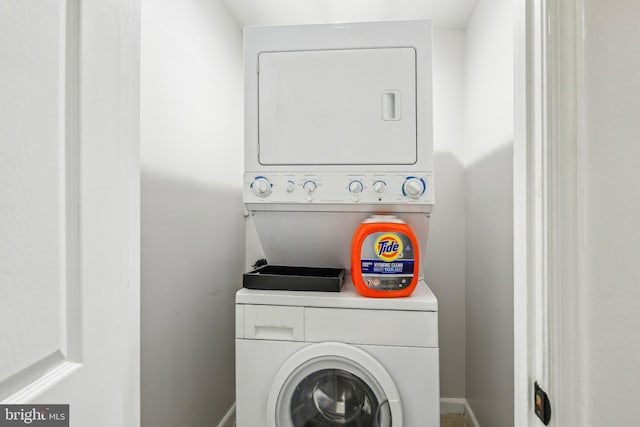 clothes washing area featuring laundry area, baseboards, and stacked washer / drying machine