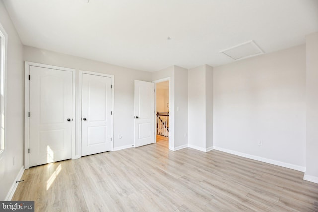 unfurnished bedroom with attic access, light wood-style flooring, and baseboards