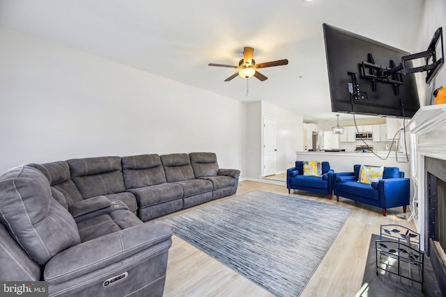 living area featuring baseboards, a fireplace with flush hearth, light wood-style floors, and ceiling fan