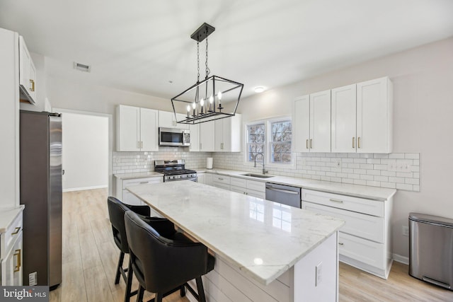 kitchen featuring visible vents, light stone countertops, decorative backsplash, appliances with stainless steel finishes, and a sink