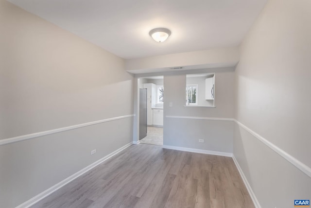 empty room featuring visible vents, light wood-type flooring, and baseboards