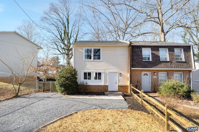 view of front of house with a gate, brick siding, roof with shingles, and fence