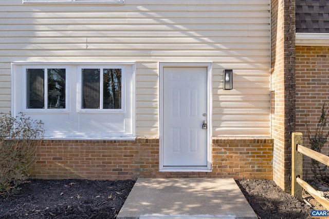 doorway to property featuring brick siding and roof with shingles