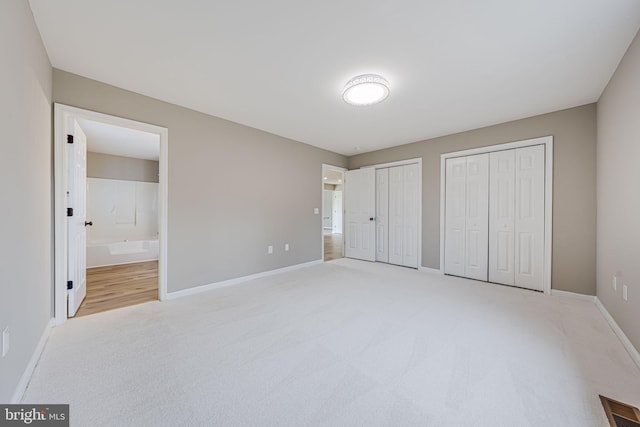 unfurnished bedroom featuring visible vents, multiple closets, light carpet, ensuite bathroom, and baseboards