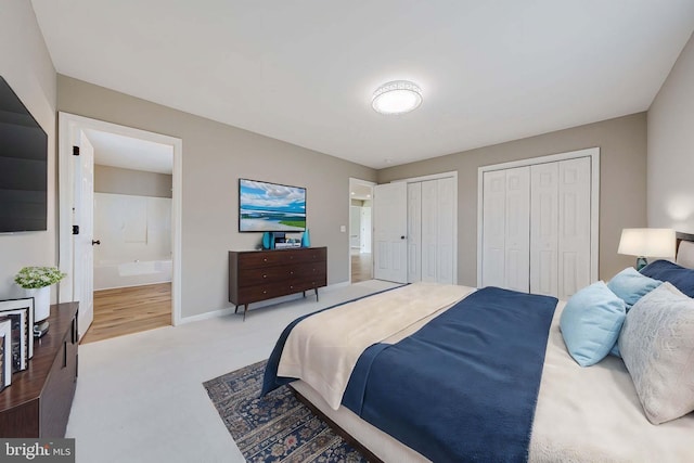 carpeted bedroom featuring baseboards, two closets, and ensuite bath