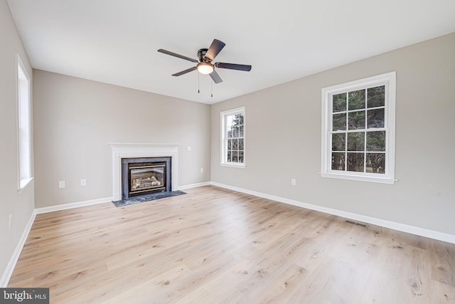 unfurnished living room with light wood-style flooring, a ceiling fan, baseboards, and a premium fireplace