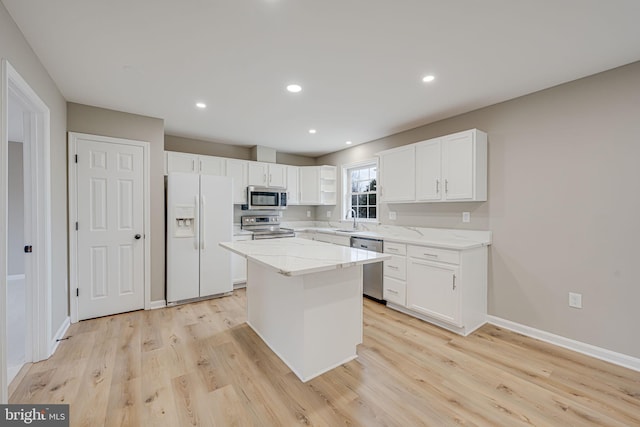 kitchen with light wood-type flooring, light stone counters, stainless steel appliances, white cabinetry, and a sink