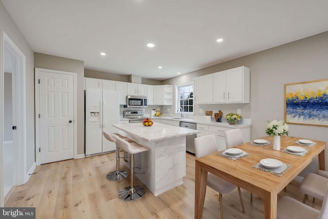 kitchen featuring a kitchen island, light wood-style flooring, stainless steel appliances, white cabinetry, and a sink