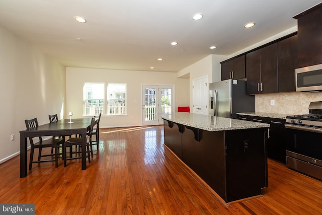 kitchen with backsplash, a center island, dark wood-type flooring, light stone countertops, and stainless steel appliances