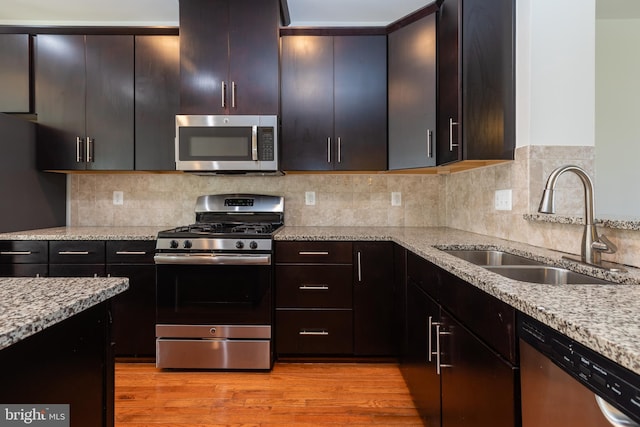 kitchen featuring light stone counters, light wood-style flooring, a sink, stainless steel appliances, and backsplash